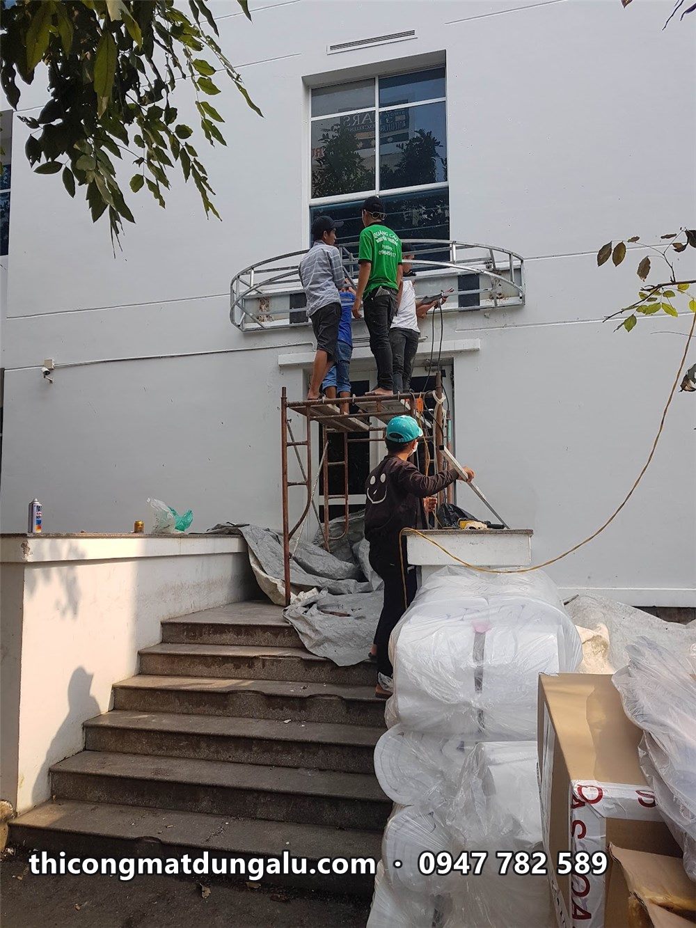 Thợ đứng trên bậc thang lắp khung mái vòm nhỏ trên cửa phụ