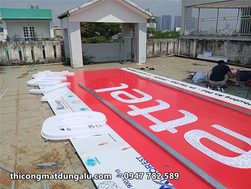 Mặt alu đỏ lớn với các chữ nổi trắng đặt cạnh, chuẩn bị gắn lên mặt