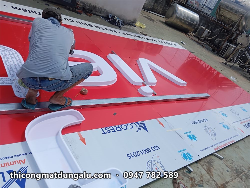 Thợ gắn chữ v trắng lên mặt alu đỏ còn màng bảo vệ