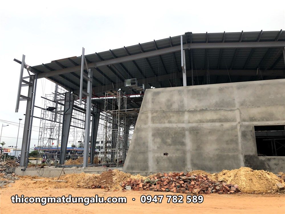 Khung thép showroom với mảng tường bê tông ở góc, đất đá ngổn ngang phía trước