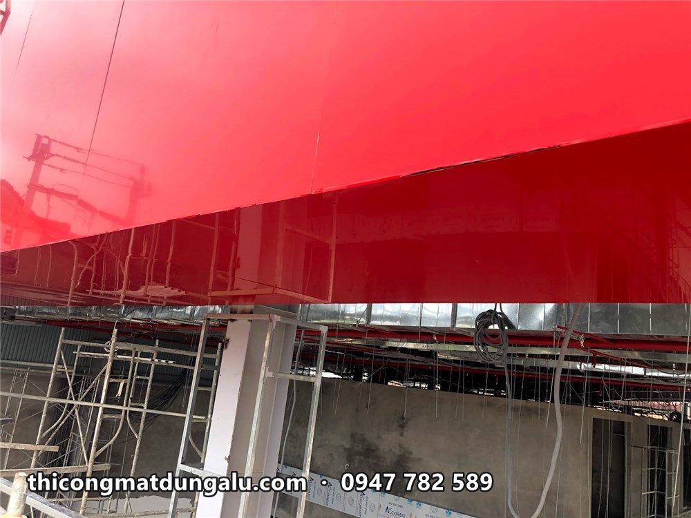 Cận cảnh tấm alu đỏ bóng ốp trên dải mái cong, giàn giáo bên dưới