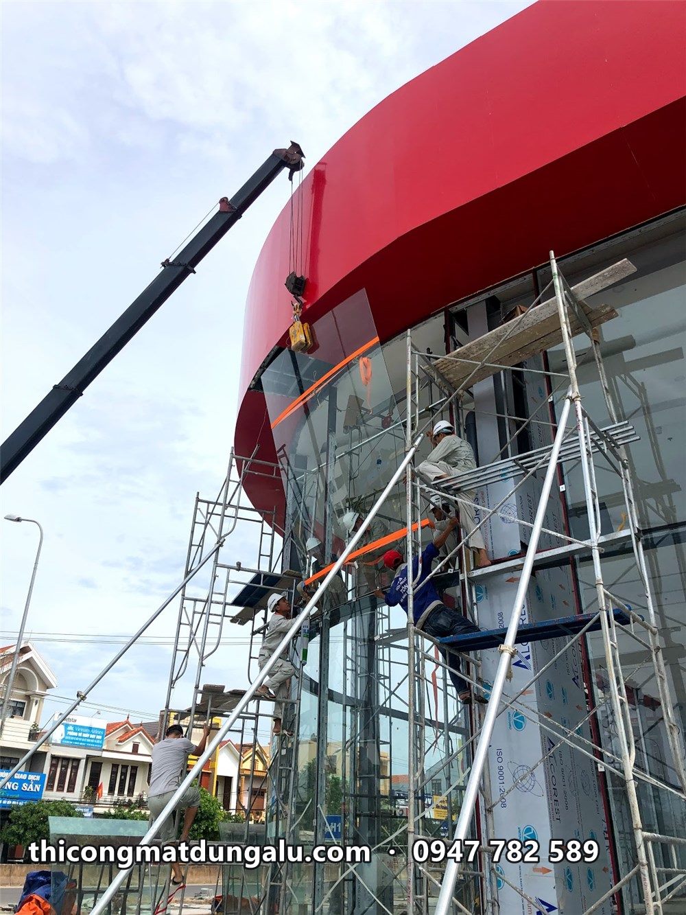 Xe cẩu và thợ trên giàn giáo ốp alu đỏ ở đoạn mái cong góc showroom