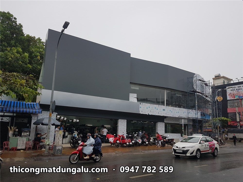 Showroom góc đường với mảng tường xám đậm phía trên đang ốp, xe cộ trên đường