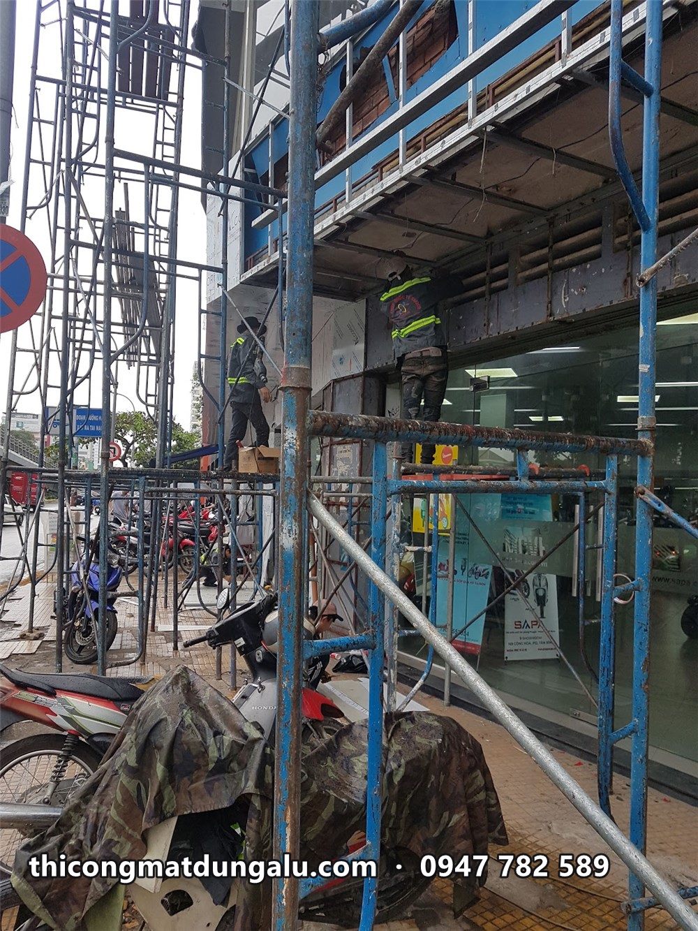 Thợ trên giàn giáo nhiều tầng trước mặt tiền showroom, xe máy đậu bên dưới