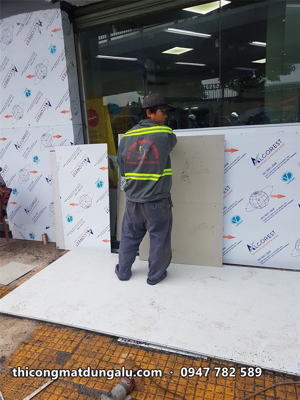 Thợ mặc áo phản quang đặt tấm alu trắng sát vách kính tầng trệt showroom