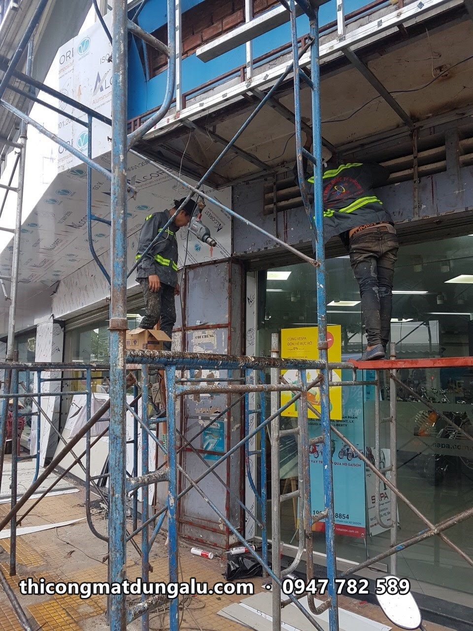 Thợ trên giàn giáo ốp tấm ở cột góc mặt tiền showroom