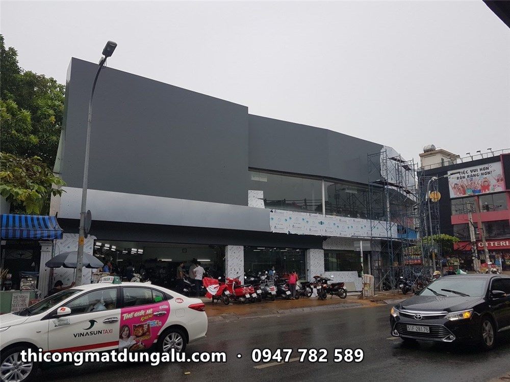 Mặt tiền showroom góc đường với mảng xám đậm đã ốp, giàn giáo đã tháo một phần