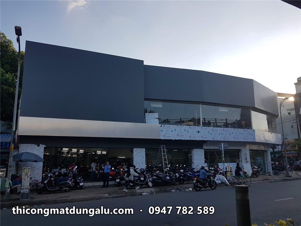 Showroom góc đường hoàn thiện, khối xám đậm phía trên và dải xám bạc ôm hàng kính