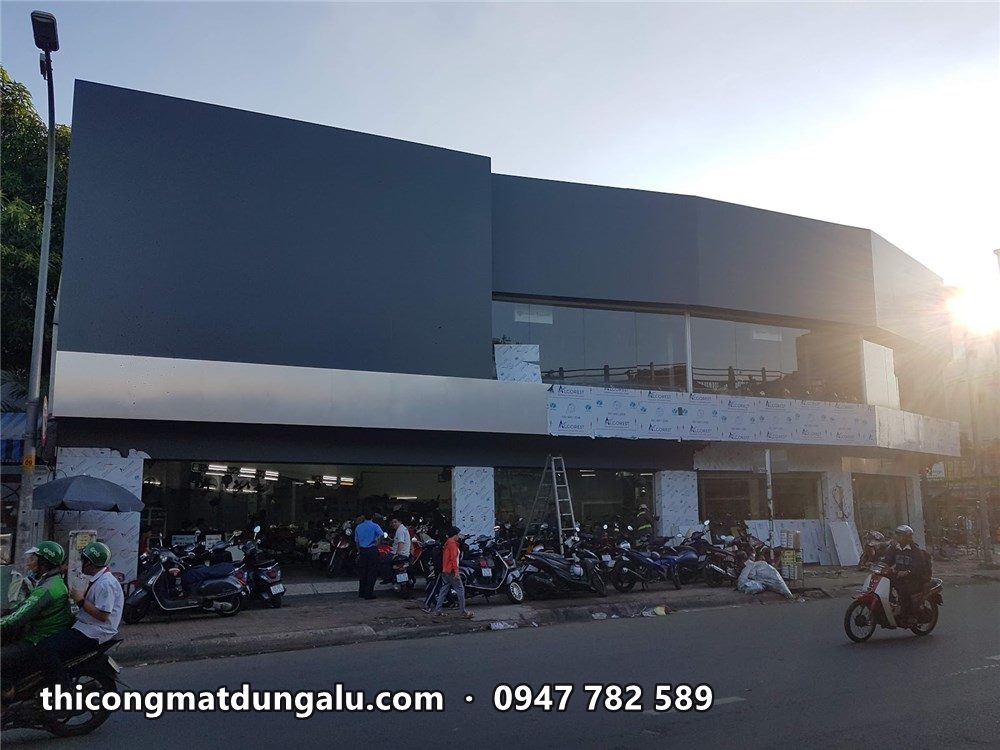 Mặt tiền showroom alu xám lúc nắng tắt, xe máy chạy qua