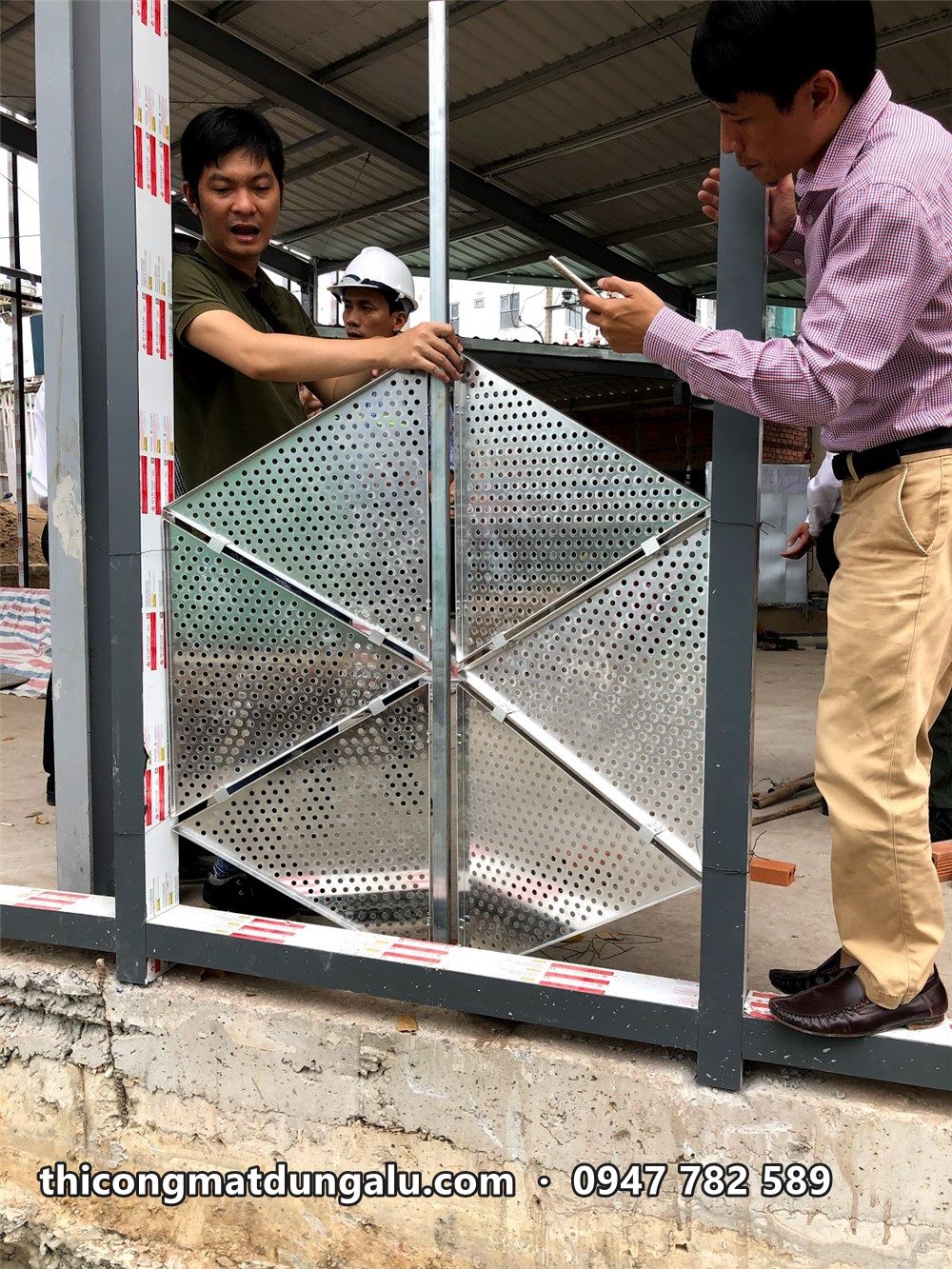 Hai người cầm tấm mẫu nhôm đục lỗ ghép hình thoi trên khung thử tại công trường
