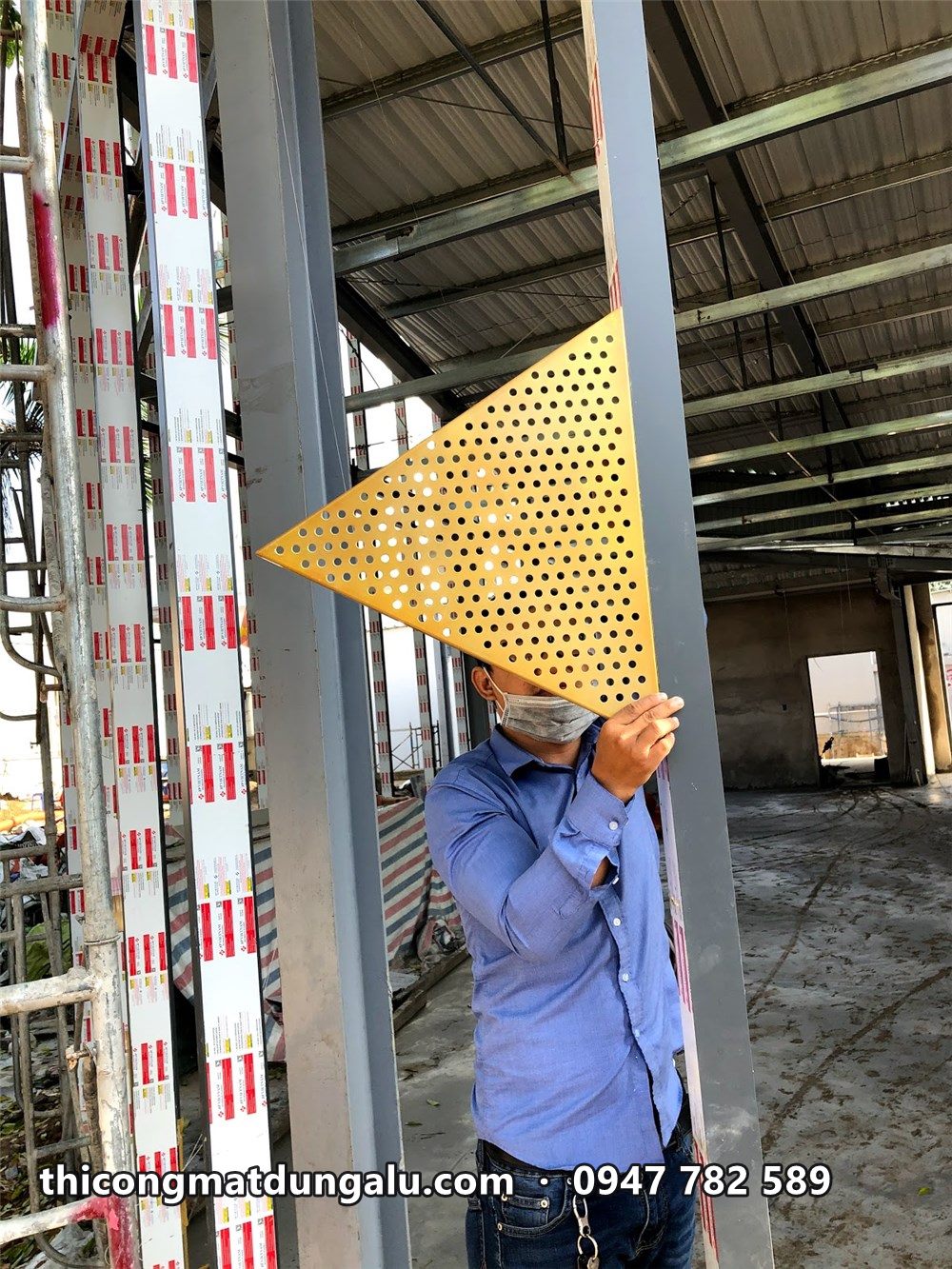 Thợ trên giàn giáo nâng tấm tam giác đục lỗ màu vàng vào vị trí