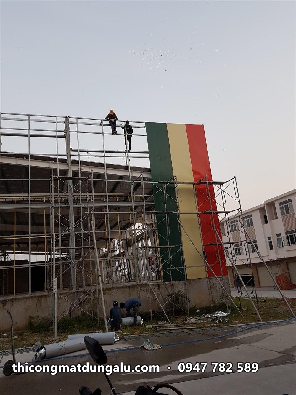 Thợ trên giàn giáo lắp những sọc tôn màu đầu tiên ở góc trung tâm thương mại