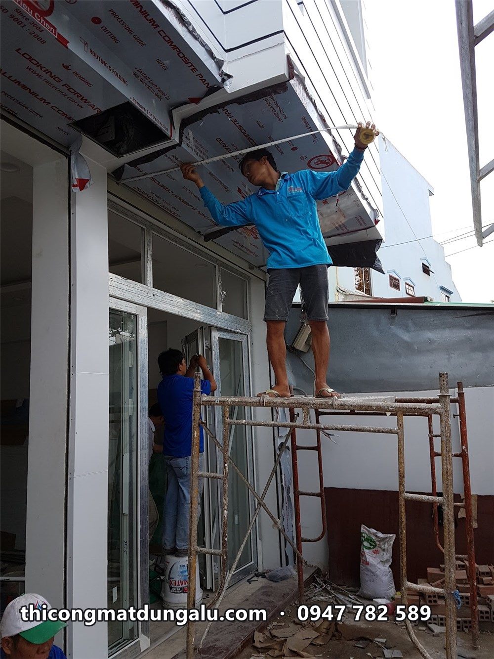 Thợ đứng trên giàn giáo lắp khung trên cửa kính bưu cục