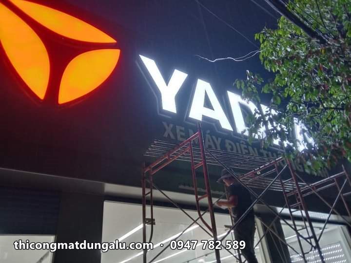 Logo YADEA cam và chữ trắng phát sáng ban đêm, thợ trên giàn giáo