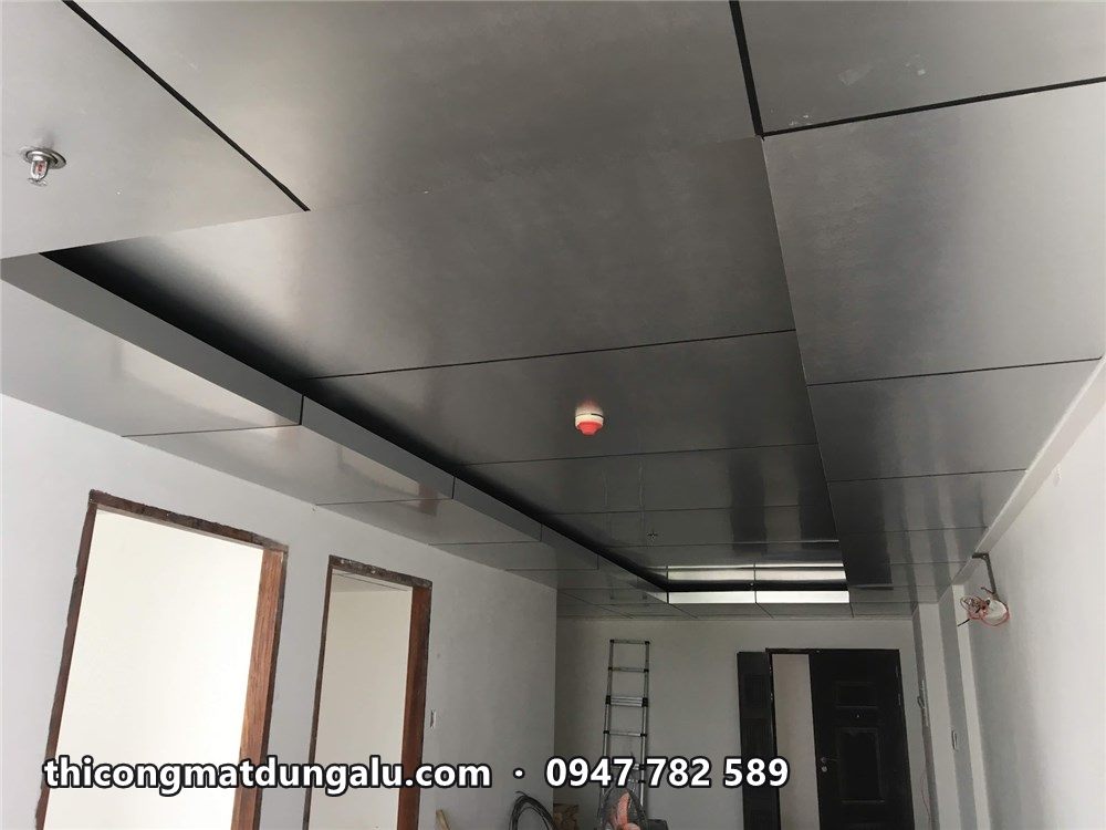 Góc phòng với trần alu bạc và đèn tuýp, cửa gỗ phía dưới