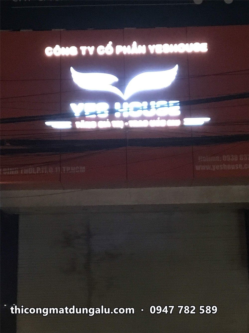 Logo đôi cánh và chữ YesHouse phát sáng trắng trên nền cam ban đêm