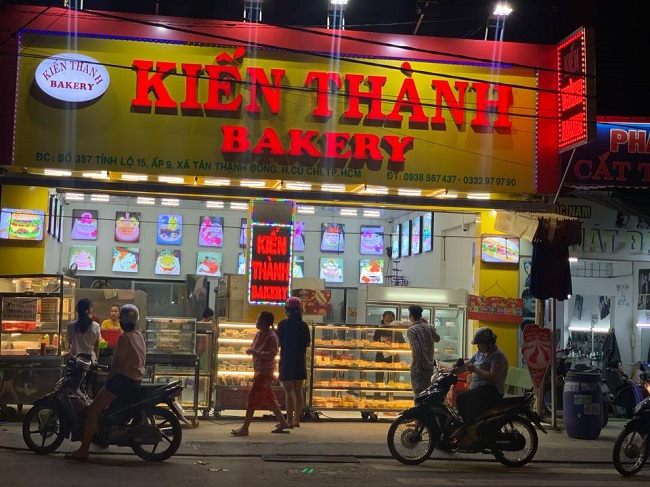 Tiệm bánh về đêm, bảng hiệu nền vàng chữ nổi đỏ và hộp đèn dọc