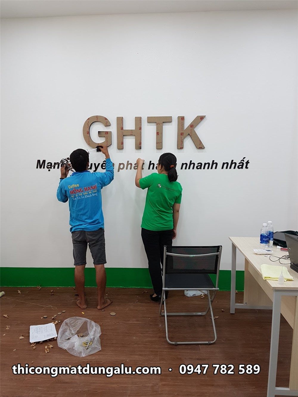 Hai thợ gắn chữ GHTK lên tường trắng trong bưu cục
