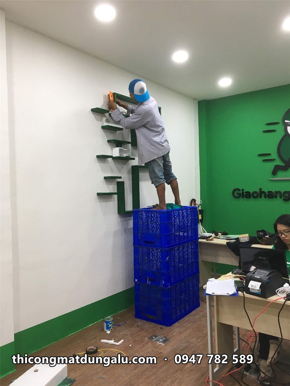 Thợ đứng trên thùng nhựa gắn các thanh của chữ F lên tường trắng