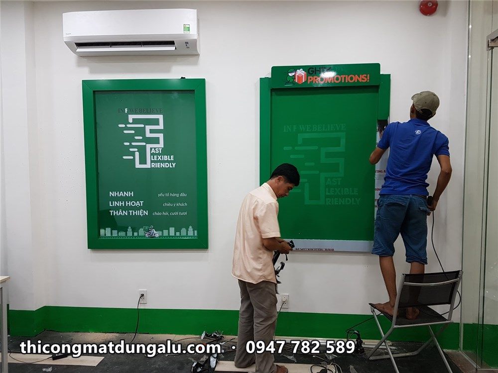 Hai thợ treo khung tranh xanh lên tường bưu cục