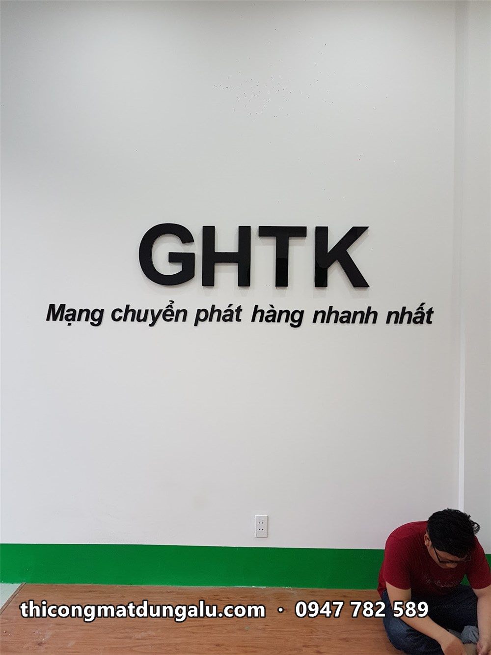 Chữ GHTK trên tường trắng, thợ ngồi dọn dẹp bên dưới
