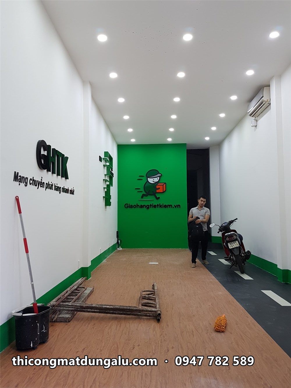 Bưu cục dài hẹp, chữ GHTK bên trái và tường xanh ở cuối, sàn kẻ vạch