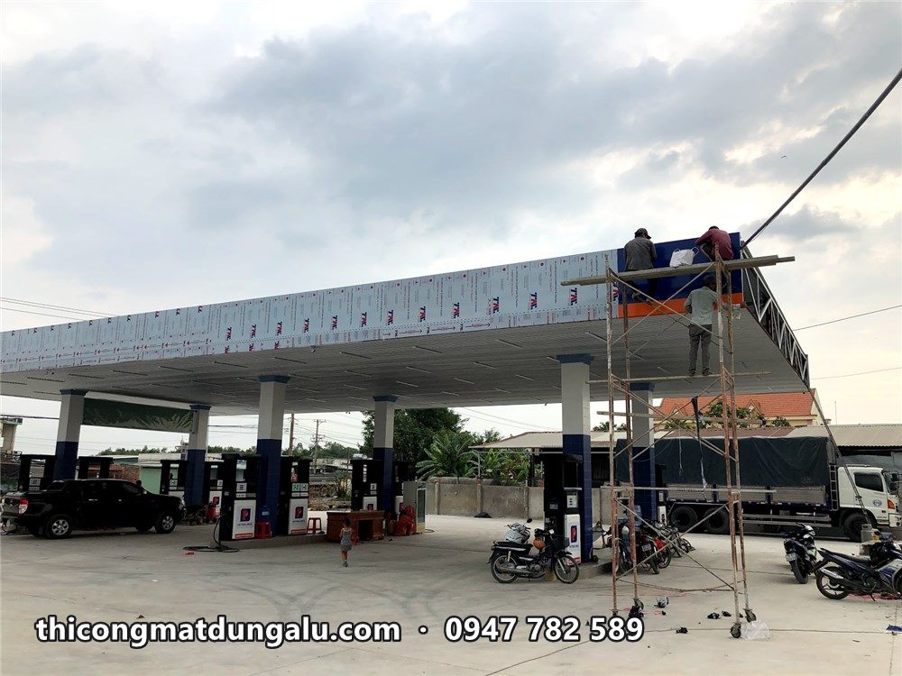 Thợ trên giàn giáo di động ốp viền mái che, cột bơm xăng phía dưới