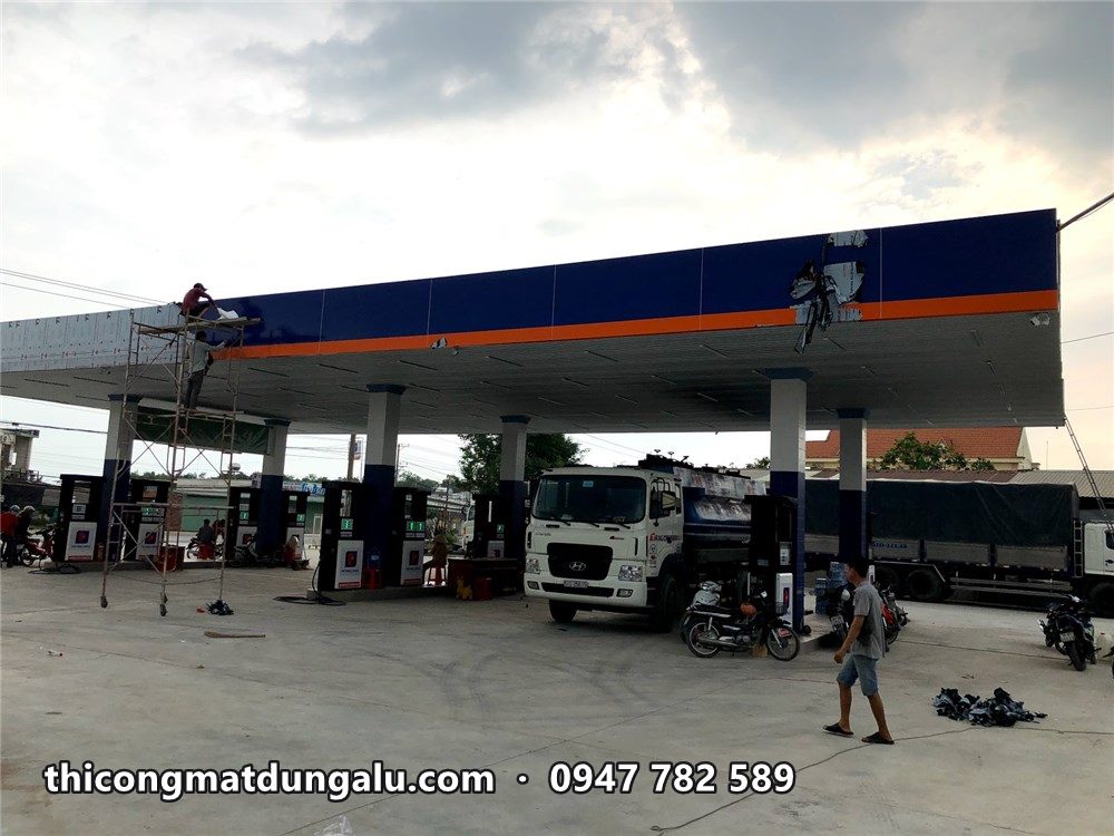 Viền mái che với dải xanh đậm và vạch cam đang lắp, thợ trên giàn giáo