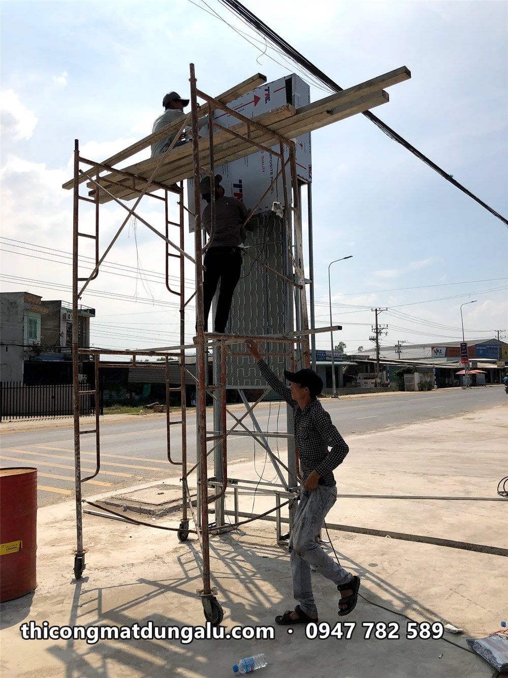 Thợ trên giàn giáo ốp tấm cho trụ giá ở lối vào cửa hàng xăng dầu