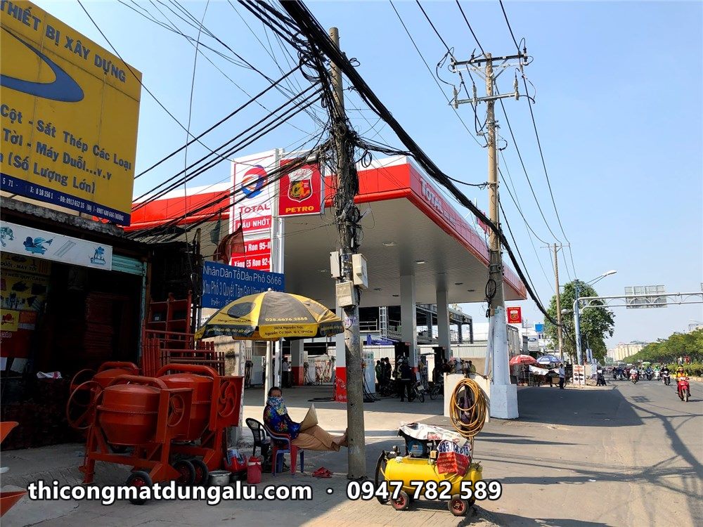 Cửa hàng xăng dầu mái viền đỏ nhìn từ vỉa hè, máy móc thi công phía trước