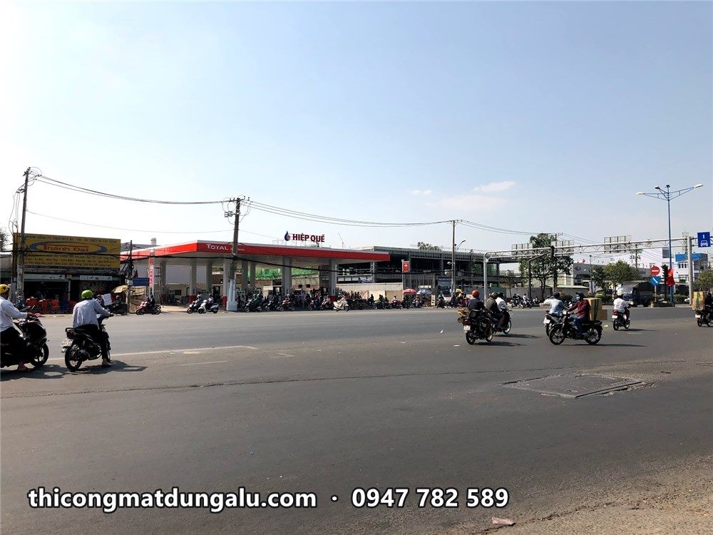 Cửa hàng xăng dầu mái viền đỏ nhìn từ bên kia quốc lộ, xe máy chạy qua
