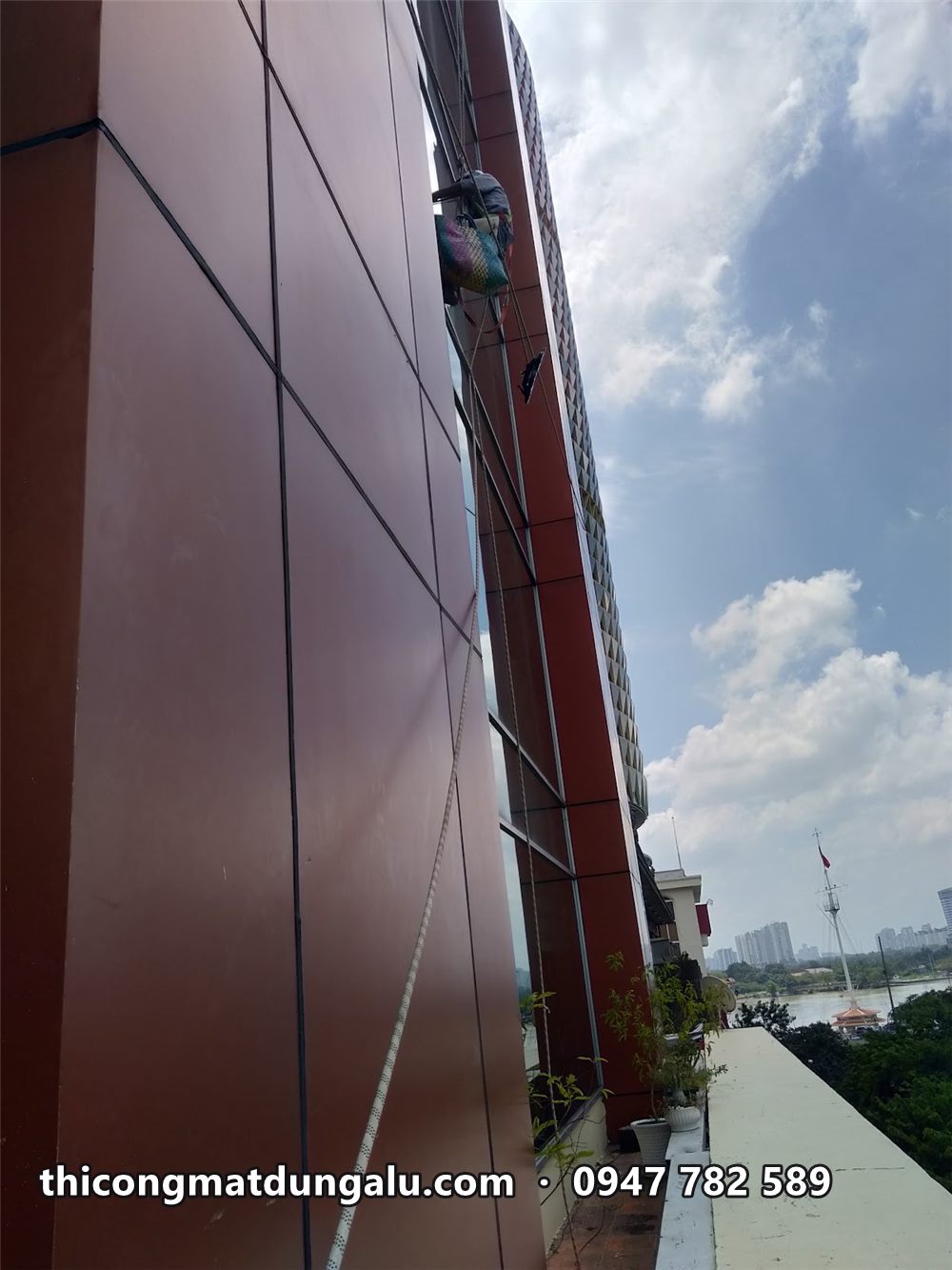 Mảng alu nâu đỏ chạy dọc tòa nhà, thợ đu dây phía trên
