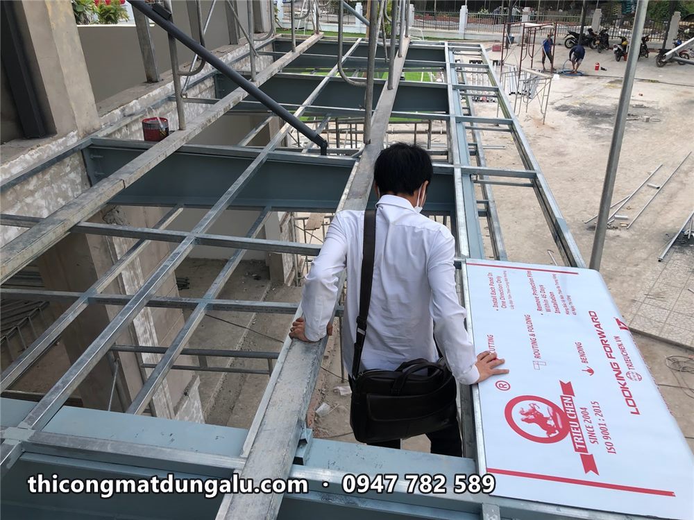Khung thép mái đón đang dựng, bên cạnh là tấm alu còn dán màng bảo vệ