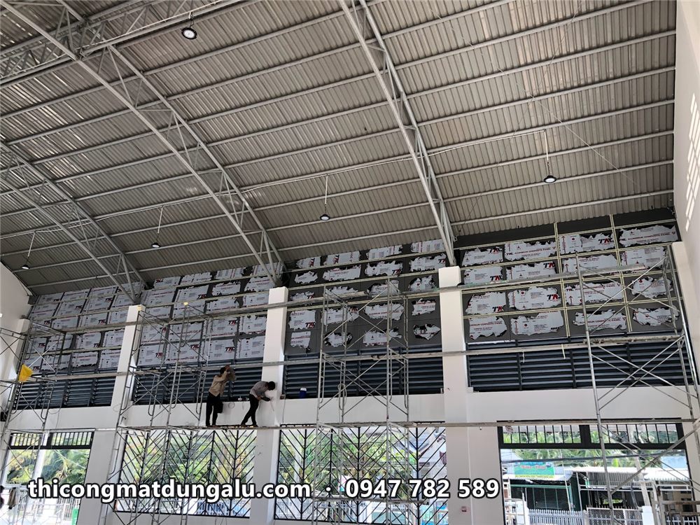 Thợ trên giàn giáo ốp alu mảng tường cao trong nhà thi đấu