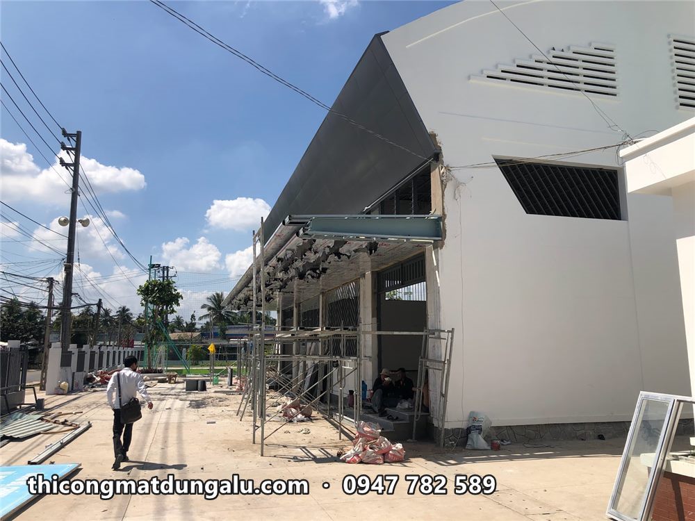 Mặt bên nhà thi đấu với mái đón ốp alu và sân trường phía trước