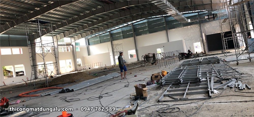 Sảnh showroom rộng còn thô, sàn chưa lát, vật tư khung xương để trên sàn