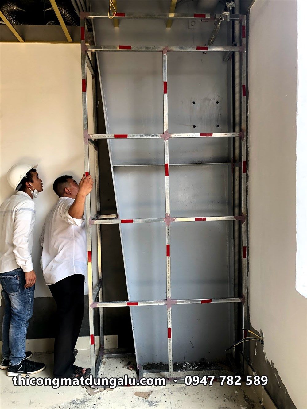 Hai thợ kiểm tra khung xương kẽm bọc quanh cột trong showroom
