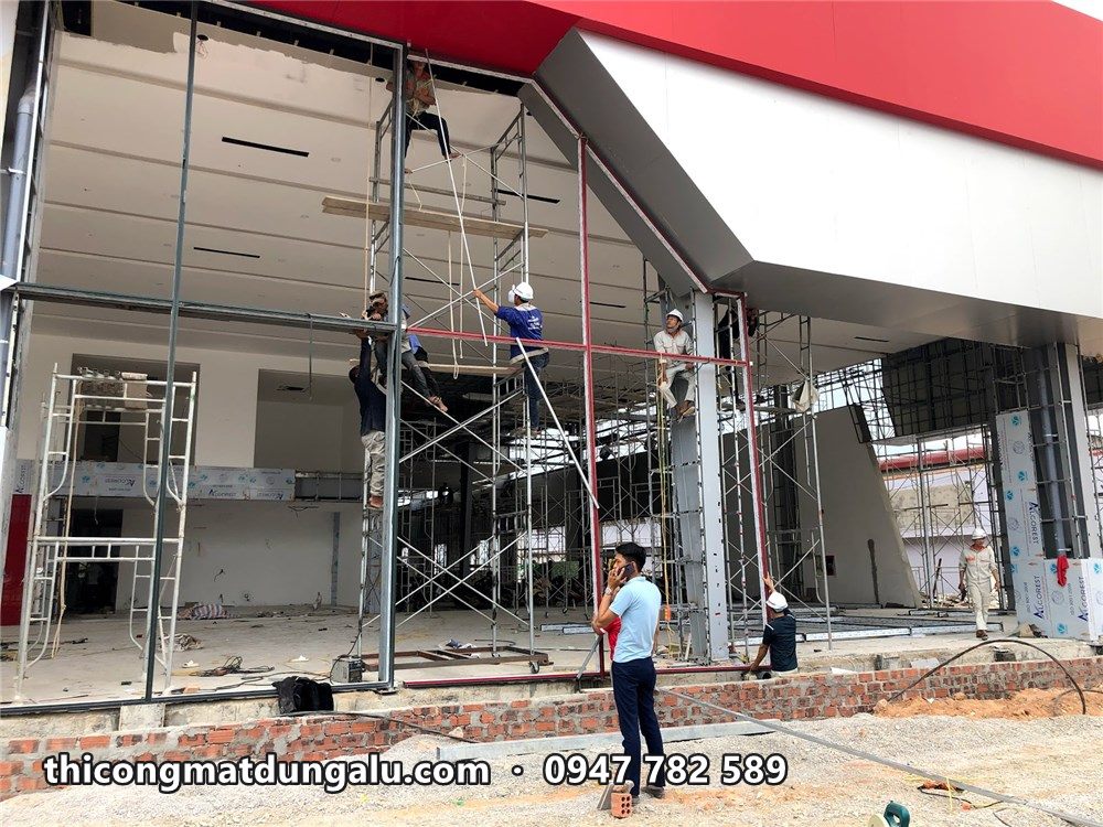 Thợ trên giàn giáo lắp khung ở mặt kính lối vào showroom, dải đỏ phía trên