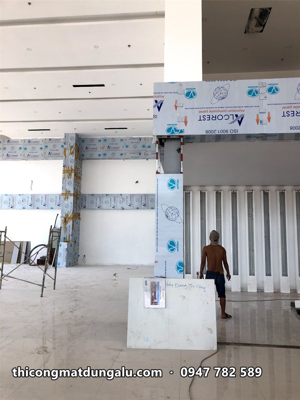 Khung cổng trong showroom đang ốp alu trắng, tấm còn màng bảo vệ in chữ