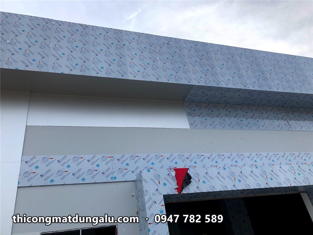 Mặt ngoài xưởng ốp alu trắng xám, tấm còn màng, điểm nhấn đỏ ở cửa