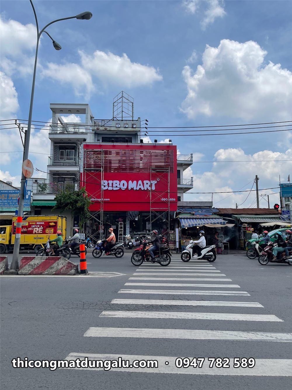Bảng Bibo Mart đỏ phủ tầng trên căn nhà ở ngã tư, vạch qua đường phía trước