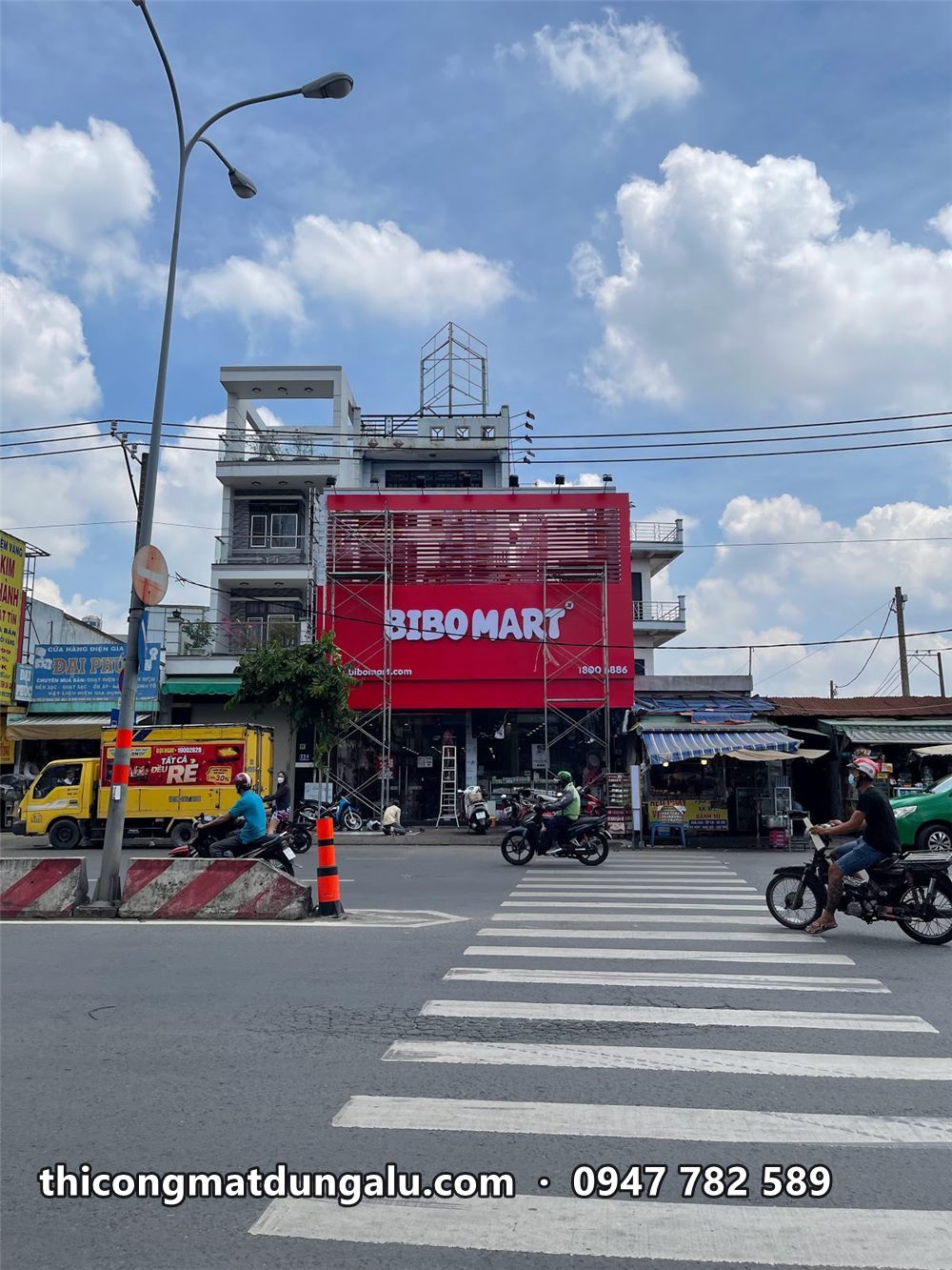 Bảng đỏ Bibo Mart trên nhà phố, xe máy dừng đèn đỏ phía dưới