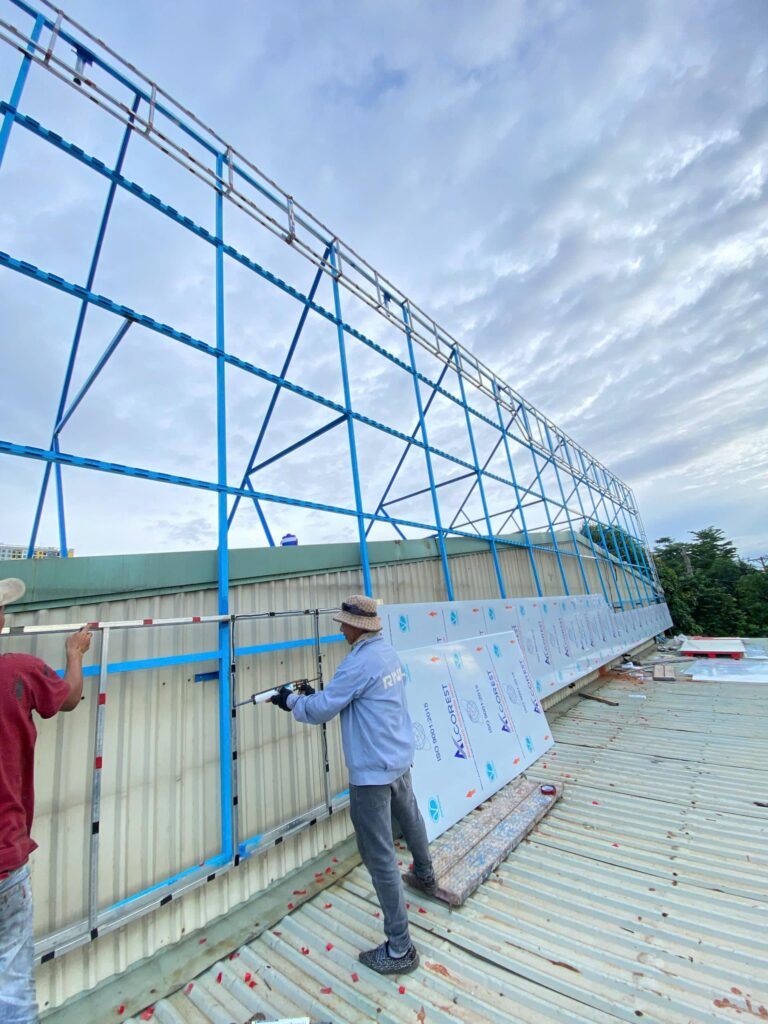 Thợ đứng trên mái tôn lắp tấm ốp lên khung thép pano sơn xanh