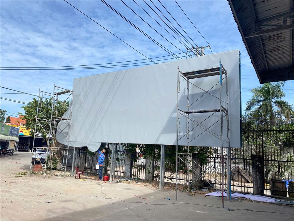 Pano dựng trụ ven đường đang lắp tấm alu trắng, giàn giáo dựng bên cạnh