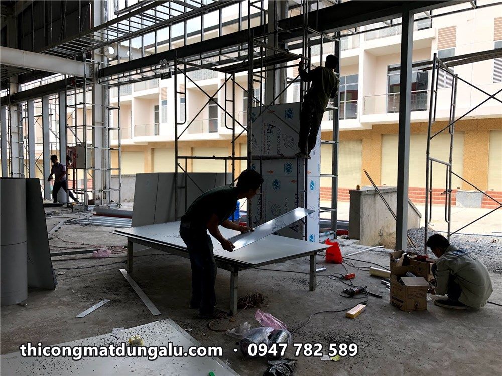 Thợ gia công tấm alu trên bàn đặt ngay trong công trình, phía sau là khung khối sảnh
