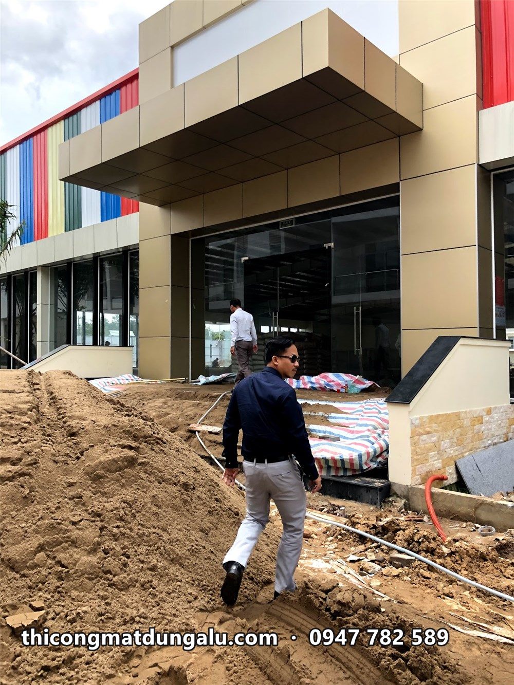 Khối sảnh ốp alu màu kem nhìn từ bên hông, công trường còn đất cát