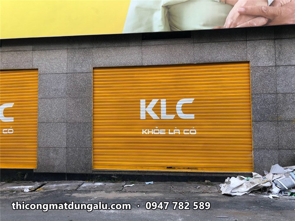 Cửa cuốn vàng có logo KLC Khỏe Là Có, mảng tường đá hai bên