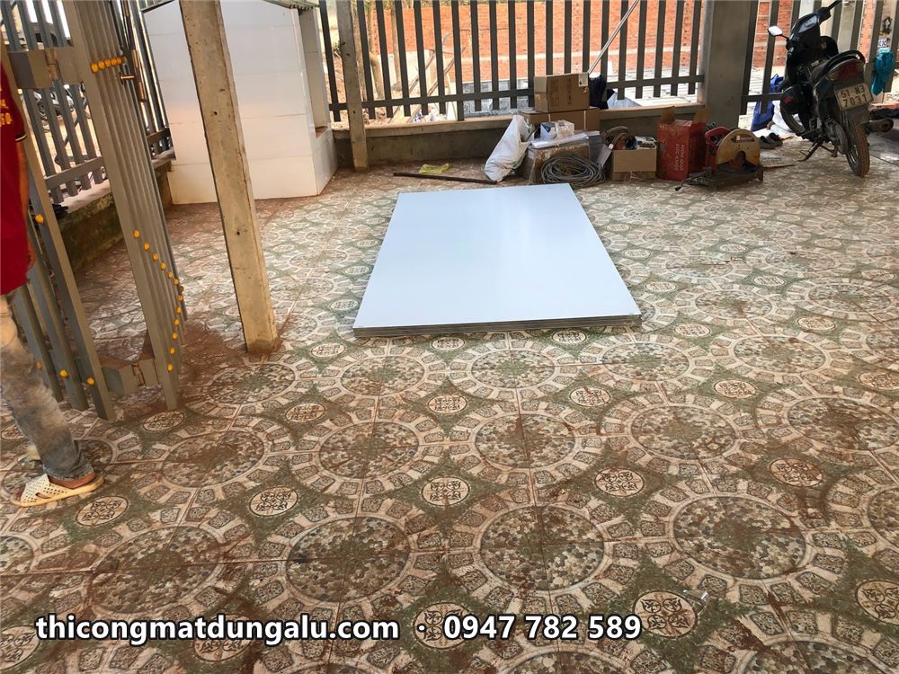 Tấm alu trắng đặt trên sàn gạch hoa, chuẩn bị cắt để ốp trần