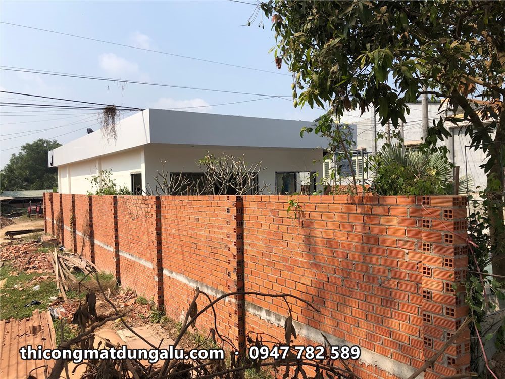 Nhà vườn mái trắng nhìn từ ngoài tường rào gạch, cây xanh phía sau