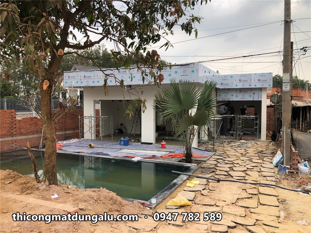 Nhà vườn với viền mái alu trắng, hồ bơi, lối đi đá và cây cọ phía trước